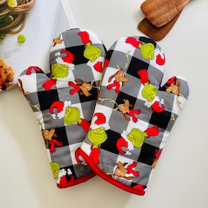 May include: A pair of oven mitts with a black and white checkered pattern. The mitts feature a red trim and are decorated with cartoon characters in red Santa hats. The characters are green and brown.