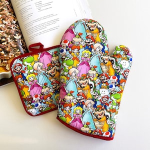 May include: A colorful oven mitt and pot holder set featuring a vibrant pattern of cartoon characters. The set has a red trim. The pot holder is square, and the oven mitt is shaped for the hand. The background is white.