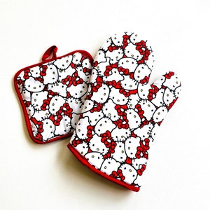 May include: A white oven mitt and pot holder set featuring a repeating pattern of a cartoon cat with a red bow. The edges of both items are trimmed with red fabric.