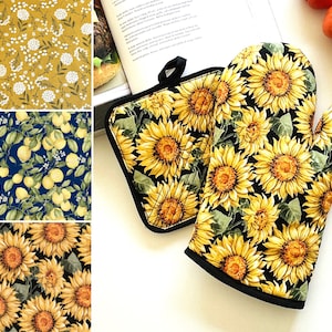 May include: A set of two oven mitts with a sunflower pattern on a black background. The mitts are made of fabric and have a black trim.