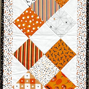 May include: A Halloween-themed table runner featuring a patchwork design with various patterns. The runner showcases orange, black, and white fabrics with motifs like pumpkins, bats, spiderwebs, and polka dots. The edges are bordered with a bat print.