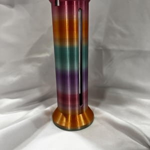 May include: A cylindrical, multi-colored 3D-printed object with a flared top and base. The colors transition from orange to green to purple. A vertical slot runs down the side of the object. The base has a circular design.