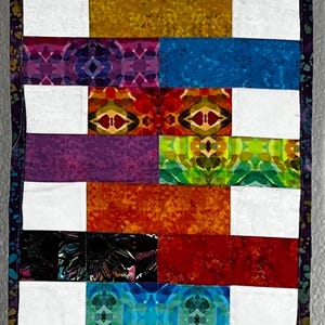 May include: A colorful, rectangular quilt with a patchwork design. The quilt features alternating rows of white squares and vibrant, patterned rectangles in shades of blue, green, red, orange, and purple. The edges are finished with a patterned border.