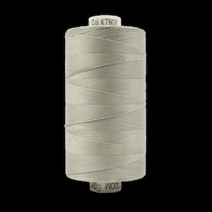 May include: A spool of light gray thread, tightly wound and cylindrical. The thread is labeled "Col. KT903" on the top and "WOOD Egy" on the bottom. The thread is a neutral color, suitable for various sewing projects.