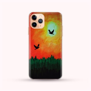May include: A clear phone case with a watercolor sunset design. The sunset is painted in shades of orange, yellow, and red. Two black silhouettes of birds are flying in the sky. The bottom of the case is painted with a dark green forest.