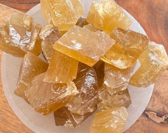 Puede incluir: Un cuenco de madera lleno de cristales de calcita dorada, rodeado de otros cristales, incluyendo amatista, y una caja de madera con una pluma.