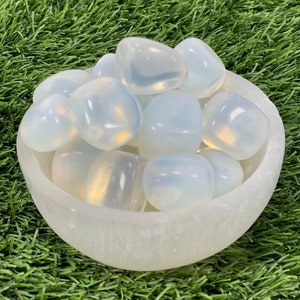May include: A white bowl filled with white opal tumbled stones. The bowl is sitting on a green grassy surface.