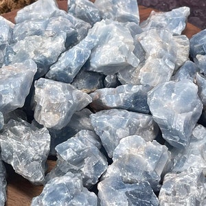 May include: A collection of blue celestite crystal chunks in various sizes and shapes. The crystals are arranged on a wooden surface.