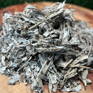 Peut inclure: Un tas de feuilles et de tiges de sauge blanche séchées sur une surface en bois. La sauge est une herbe populaire utilisée pour le smudging et la purification.
