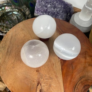 Op de afbeelding: Drie witte seleniet bollen op een houten oppervlak. De bollen zijn glad en gepolijst, met een lichte glans.