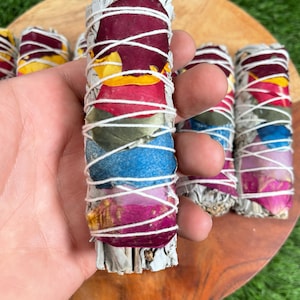 May include: A white sage smudge stick wrapped with dried rose petals in a rainbow of colors, including red, orange, yellow, green, blue, and purple.
