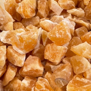 May include: A close-up of a pile of orange calcite crystals. The crystals are rough and have a natural, unpolished look.