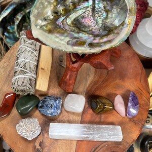 May include: A wooden tray with a variety of crystals and stones, including a selenite wand, a large abalone shell, and a sage bundle. The tray is surrounded by smaller crystals and stones.