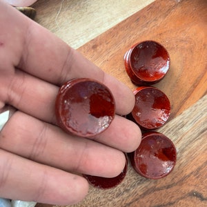 May include: Five small, round, wooden display stands with a deep red stain. The stands are designed to hold small objects, such as crystals or other decorative items.