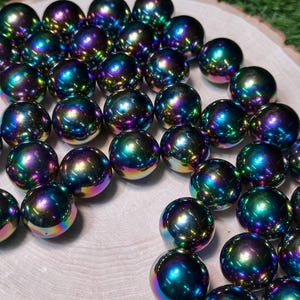 K&ouml;nnte beinhalten: Eine Ansammlung von irisierenden Kugeln mit polierter, reflektierender Oberfl&auml;che. Die Kugeln zeigen eine lebendige Farbpalette, darunter Blau-, Gr&uuml;n-, Lila- und Gelbt&ouml;ne. Sie sind auf einer hellen Holzoberfl&auml;che angeordnet.