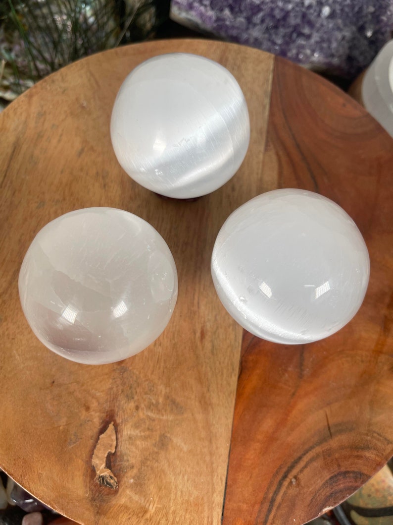 Op de afbeelding: Drie witte seleniet bollen op een houten oppervlak. De bollen zijn glad en hebben een doorschijnende uitstraling.