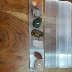 May include: A set of seven tumbled stones, including carnelian, amethyst, green aventurine, tiger's eye, rose quartz, red jasper, and a white agate, arranged on a selenite charging plate.