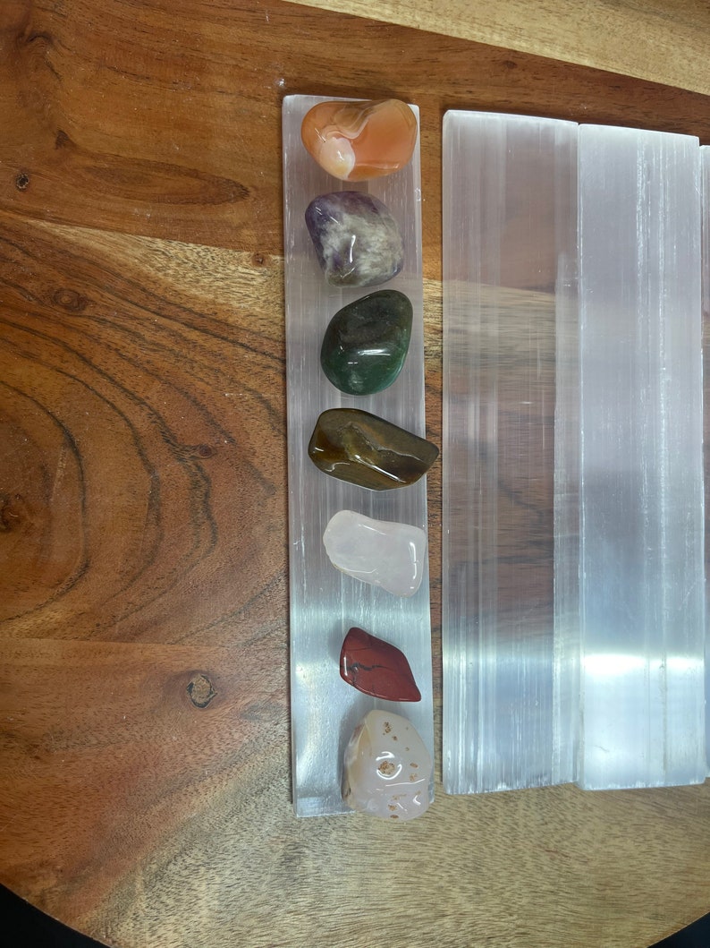May include: A set of seven tumbled stones, including carnelian, amethyst, green aventurine, tiger's eye, rose quartz, red jasper, and a white agate, arranged on a selenite charging plate.