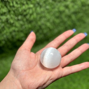 Op de afbeelding: Een witte selenietbol, ook wel bekend als maansteen, wordt in een hand gehouden. De bol is glad en heeft een doorschijnende uitstraling.