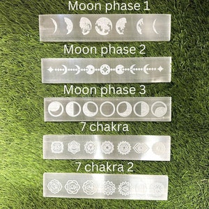 May include: Five white crystal wands with etched moon phases and chakra symbols. The wands are arranged vertically on a green grassy surface. The text on the wands reads "Moon phase 1", "Moon phase 2", "Moon phase 3", "7 chakra", and "7 chakra 2".