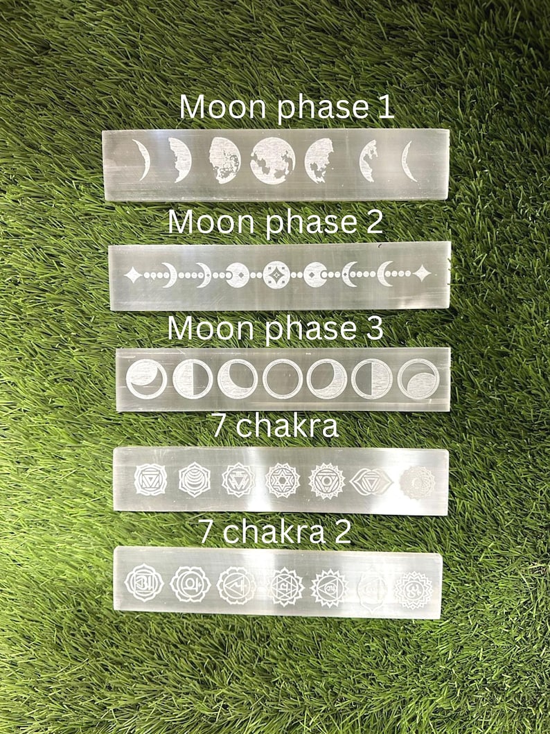 May include: Five white crystal wands with etched moon phases and chakra symbols. The wands are arranged vertically on a green grassy surface. The text on the wands reads "Moon phase 1", "Moon phase 2", "Moon phase 3", "7 chakra", and "7 chakra 2".