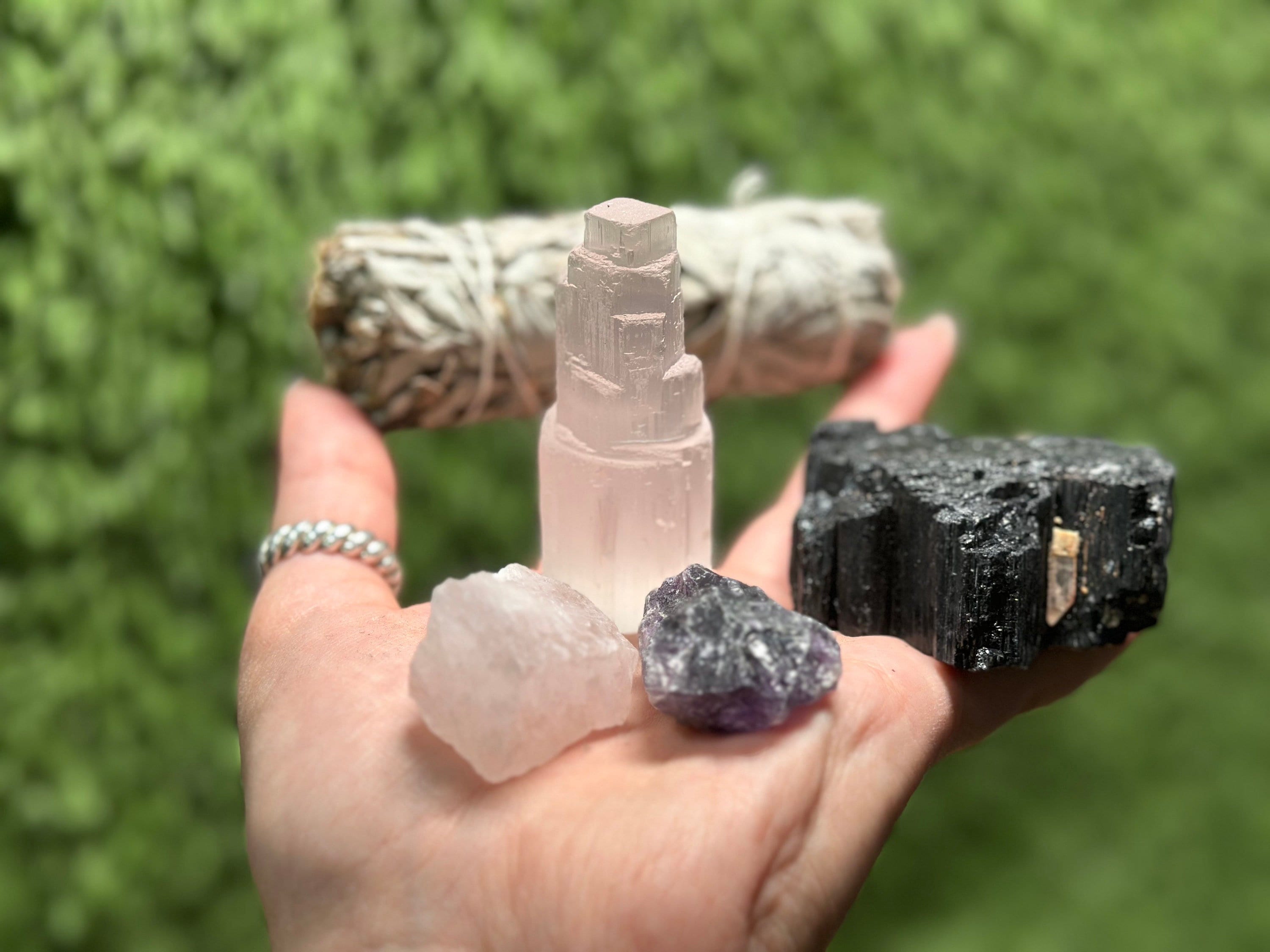 Hand holding selenite tower, black tourmaline, amethyst, and rose quartz – powerful protection crystal kit for witches.