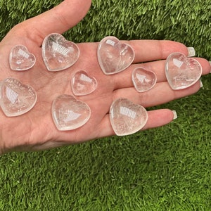 May include: A collection of clear quartz heart-shaped crystals of varying sizes. The crystals are smooth and polished, with a translucent appearance.