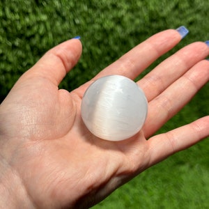 Op de afbeelding: Een witte selenietbol, ook wel een selenietkogel genoemd, wordt in een hand gehouden. De bol is glad en heeft een gestreepte textuur.