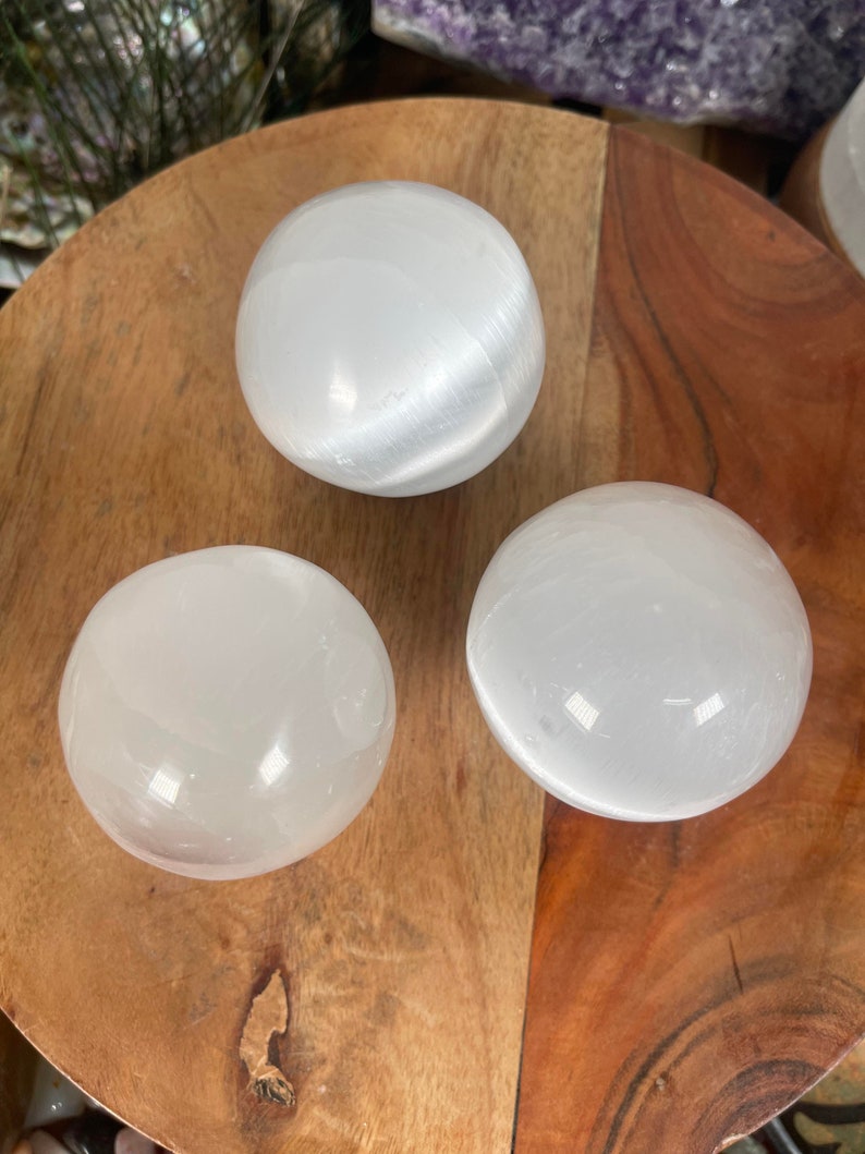 Op de afbeelding: Drie witte seleniet bollen op een houten oppervlak. De bollen zijn glad en hebben een licht iriserende glans.