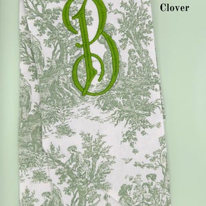 May include: A white fabric with a green toile pattern and a green embroidered letter "B" in the Penelope font. The text "Font: Penelope Color: Clover" is visible in the upper right corner of the image.