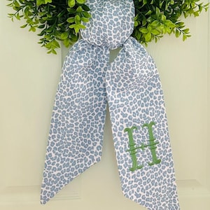 May include: A blue and white leopard print fabric bow with a green embroidered letter "H" in the center.