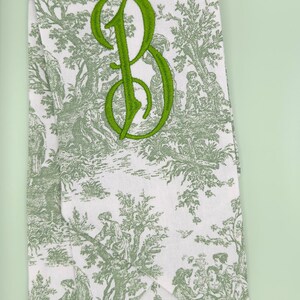 May include: A white fabric tea towel with a green toile pattern and a green embroidered letter "B".