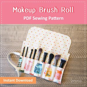 May include: A fabric makeup brush roll featuring a white base with colorful milk carton illustrations and a flap patterned with small orange and yellow hearts. The roll contains eight makeup brushes with black handles and dark bristles.