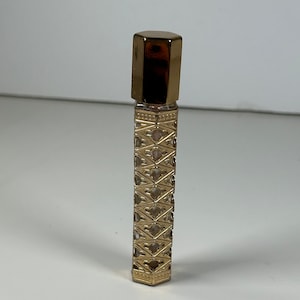 May include: A gold-colored glass perfume bottle with a decorative pattern and a gold-colored cap.