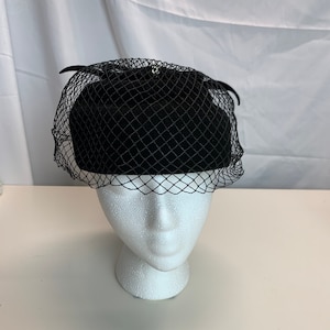May include: A black felt hat with a black net veil. The hat is on a white mannequin head.