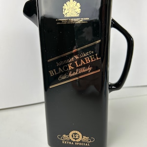 May include: Black ceramic jug with a gold Johnnie Walker Black Label logo and the text "Old Scotch Whisky". The jug also has a gold royal crest and the text "By Appointment to Her Majesty the Queen Scotch Whisky Distillers John Walker and Sons Limited London". The bottom of the jug has a gold label with the text "12 Years Extra Special".