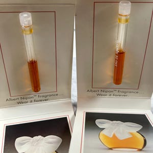 May include: Two sample vials of Albert Nipon fragrance, one labeled "Eau de Toilette". The vials are displayed on white cards with the text "Albert Nipon™ fragrance... Wear it forever."  Below the vials are images of a bottle of perfume with a white bow.