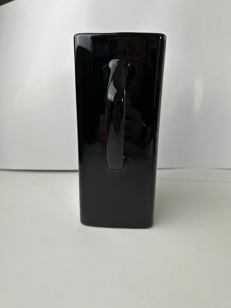 May include: A black ceramic mug with a large handle. The mug is tall and rectangular in shape.