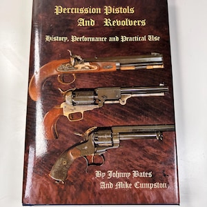 May include: A book titled "Percussion Pistols And Revolvers" with a brown cover. The cover features images of antique firearms. The text on the cover reads "History, Performance and Practical Use" and the authors are Johnny Bates and Mike Cumpston.