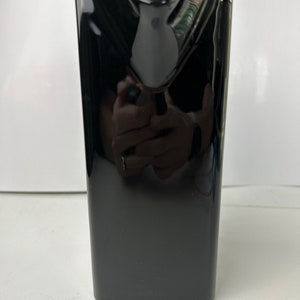 May include: A black ceramic vase with a rounded top and a small hole in the centre. The vase has a glossy finish.