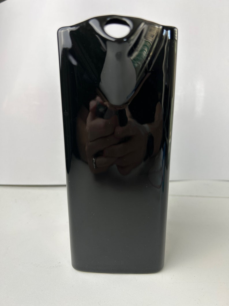 May include: A black ceramic vase with a rounded top and a small hole in the centre. The vase has a glossy finish.