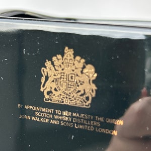 May include: A black box with a gold royal crest and the text "By Appointment to Her Majesty The Queen Scotch Whisky Distillers John Walker and Sons Limited London."