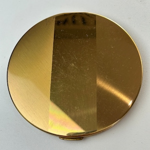 May include: A round, gold-colored compact mirror with a vertical stripe down the center.