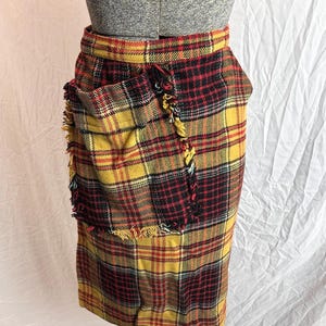 May include: A vintage plaid skirt in yellow, red, and black. The skirt features a fringed pocket and a classic plaid pattern. The skirt is displayed on a mannequin.