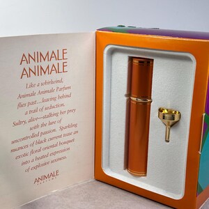 May include: A gift set featuring a cylindrical orange perfume atomizer with gold accents and a small gold funnel, housed in a box with the text ANIMALE ANIMALE and descriptive marketing copy printed on the interior left panel of the packaging.