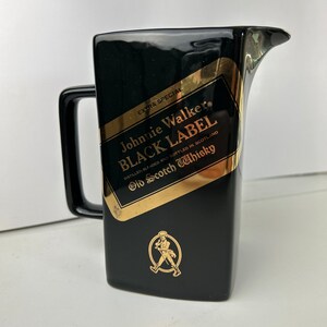 K&ouml;nnte beinhalten: Schwarzer Keramik-Krug mit goldenem Johnnie Walker Black Label Logo und einer Grafik eines laufenden Mannes. Das Etikett lautet "Extra Special", "Johnnie Walker", "Black Label", "Distilled, Blended and Bottled in Scotland", und "Old Scotch Whisky".