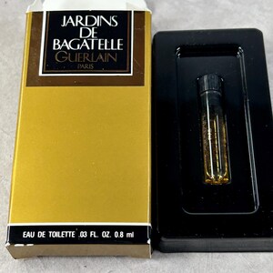 May include: A gold box with the text "JARDINS DE BAGATELLE GUERLAIN PARIS" and "EAU DE TOILETTE .03 FL. OZ. 0.8 ml" on it. A small clear glass bottle with a black cap is in a black plastic case.
