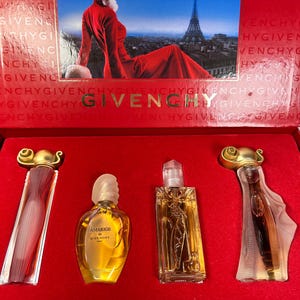 May include: A Givenchy gift set in a red box featuring an image of a person in a red dress with the Eiffel Tower. The set contains four perfume bottles: two with gold caps, one rounded bottle labeled Amarige de Givenchy, and one rectangular bottle.