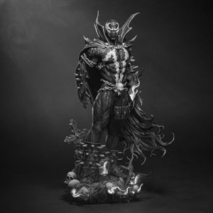 May include: Black and white statue of Spawn, a comic book character, standing on a detailed base with skulls and a cross. The figure is clad in a cape, chains, and a mask, with intricate detailing.