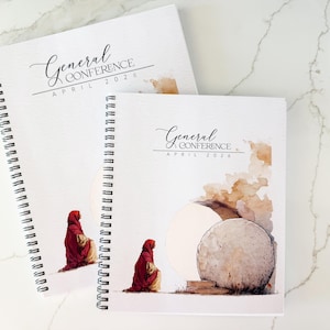 May include: Two spiral-bound notebooks with white covers. The covers feature the text "General Conference April 2026" in elegant script. One notebook has an illustration of two figures in red robes. The other notebook has an illustration of a tomb.